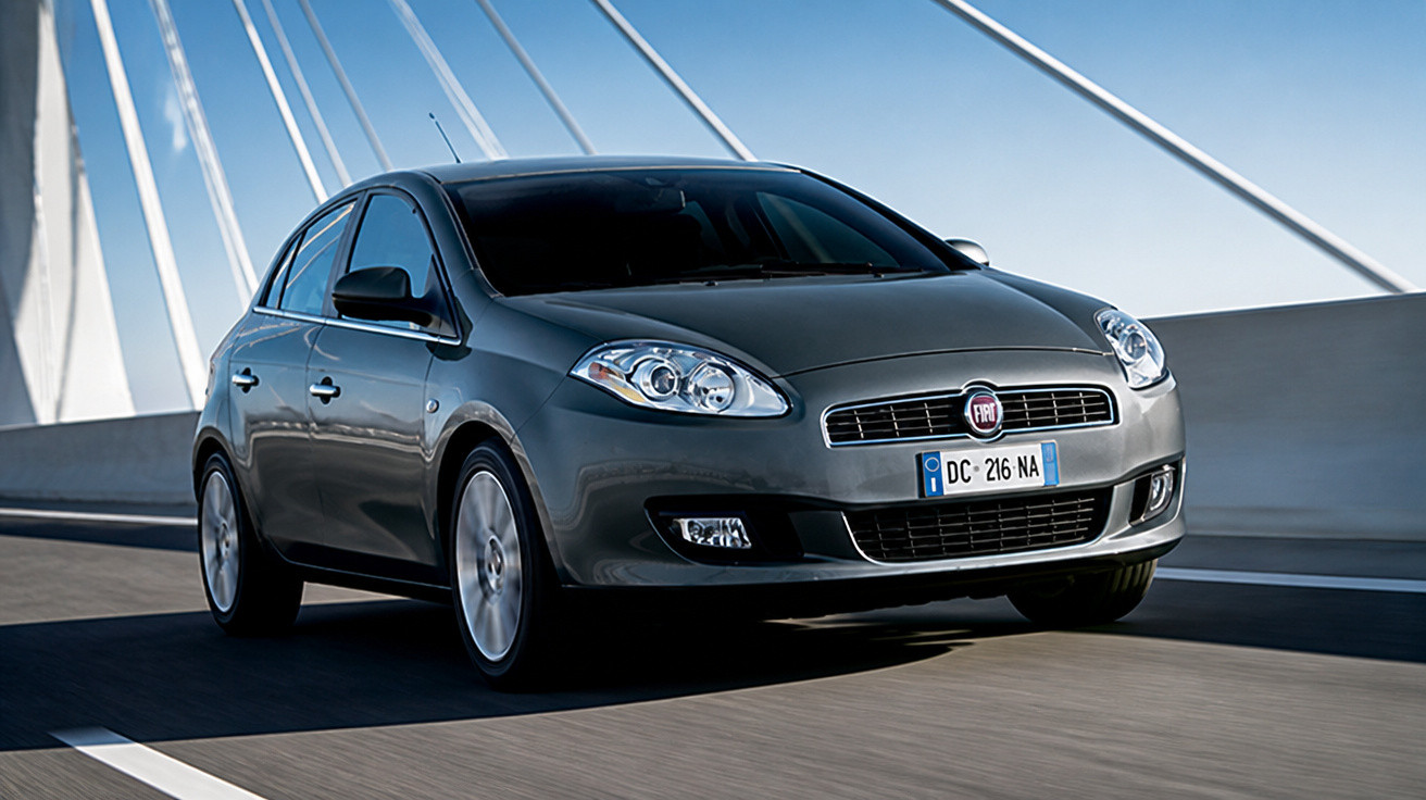 Carro cinza modelo Fiat Punto trafegando em ponte moderna com cabos tensionados ao fundo.