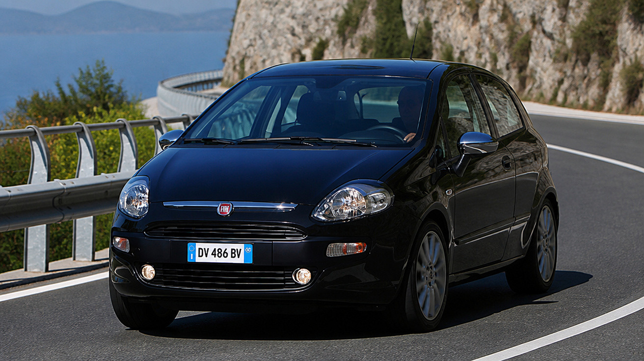 Carro preto compacto Fiat circulando em estrada sinuosa com pedras e mar ao fundo.