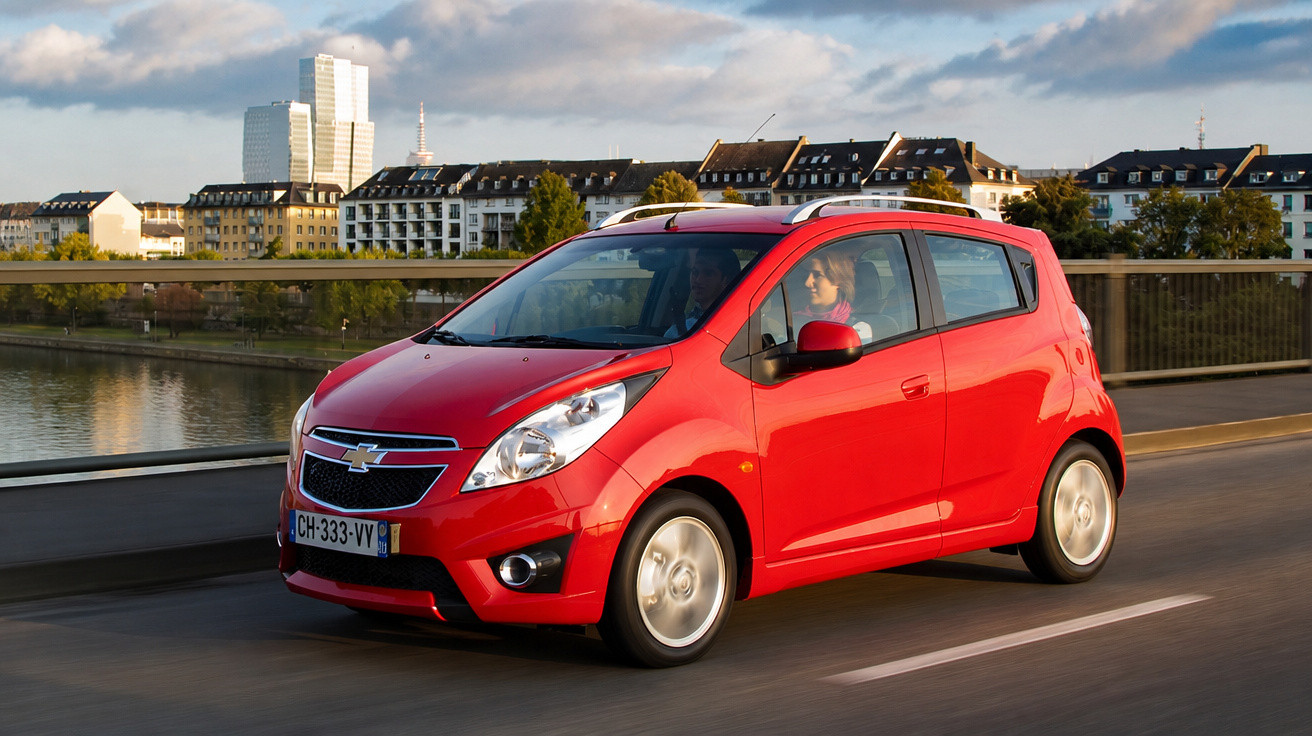 Carro vermelho Chevrolet em movimento na ponte com edifícios ao fundo em dia ensolarado.