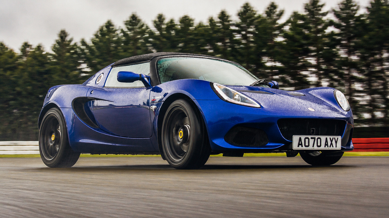 Carro esportivo azul escuro em pista de corrida com fundo de árvores e céu nublado.